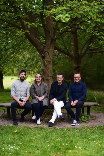 Skupinka lidí z týmu Silene sedící na lavičce v parku pod stromy.