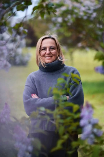 Portrét ženy (Lenky Čápové) ve světlém roláku, stojící mezi kvetoucími šeříky a usmívající se do objektivu