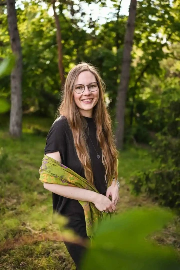 Portrét hnědovlasé ženy s brýlemi (Terezy Kadlecové) v lesním prostředí, držící zelený šátek.